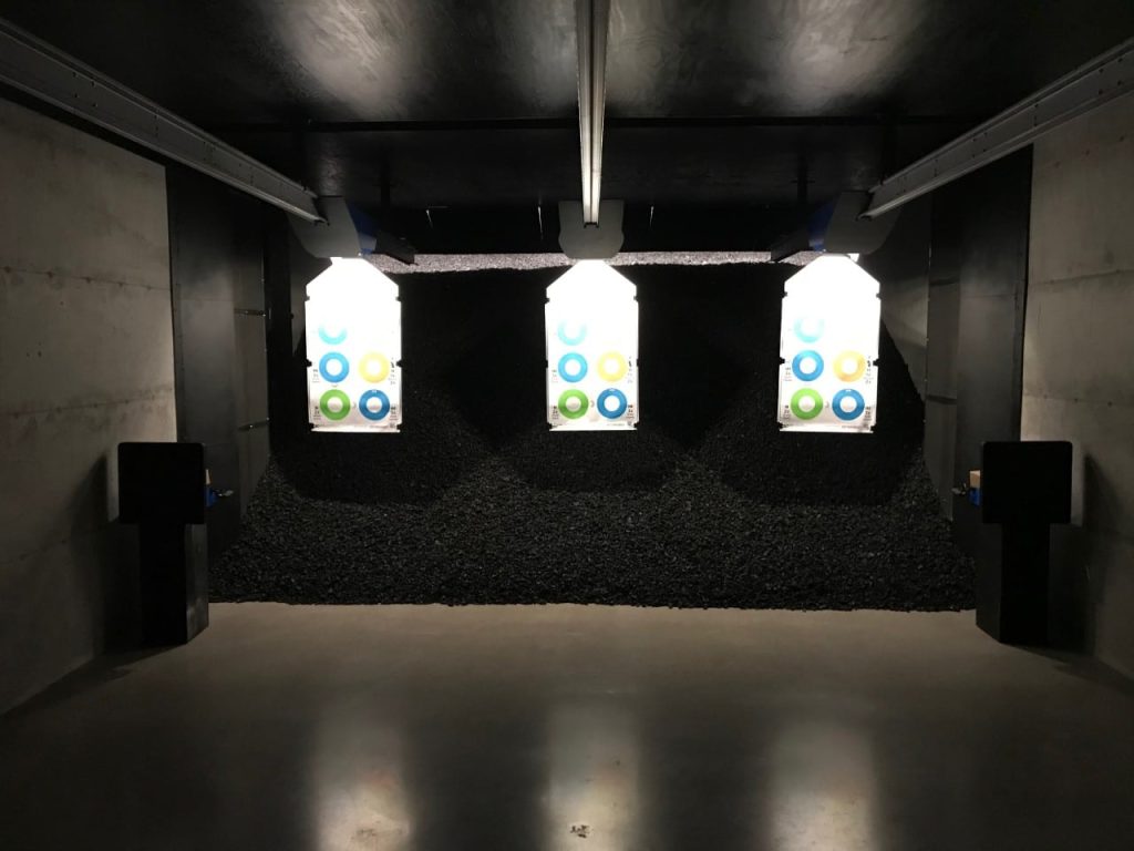 Targets with colored circles hang in a dimly lit indoor shooting range.