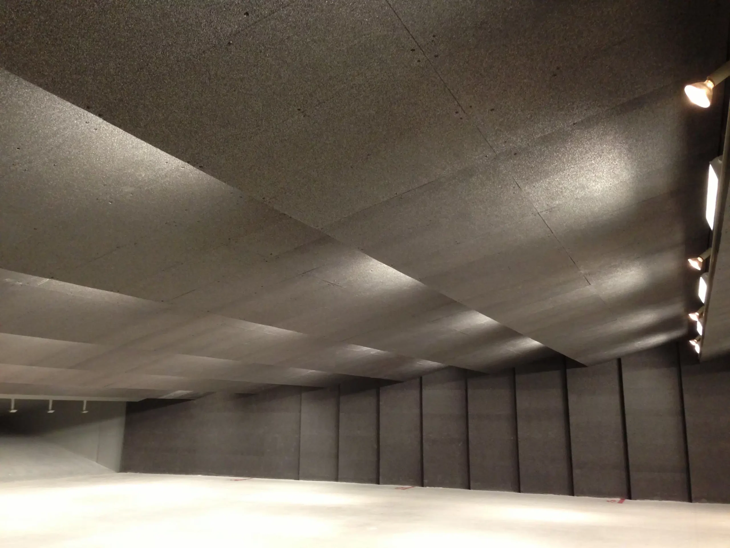 Empty indoor shooting range with lined ceiling and walls; bright light fixtures illuminate space.