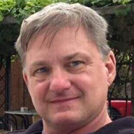 Headshot of a man smiling outdoors.