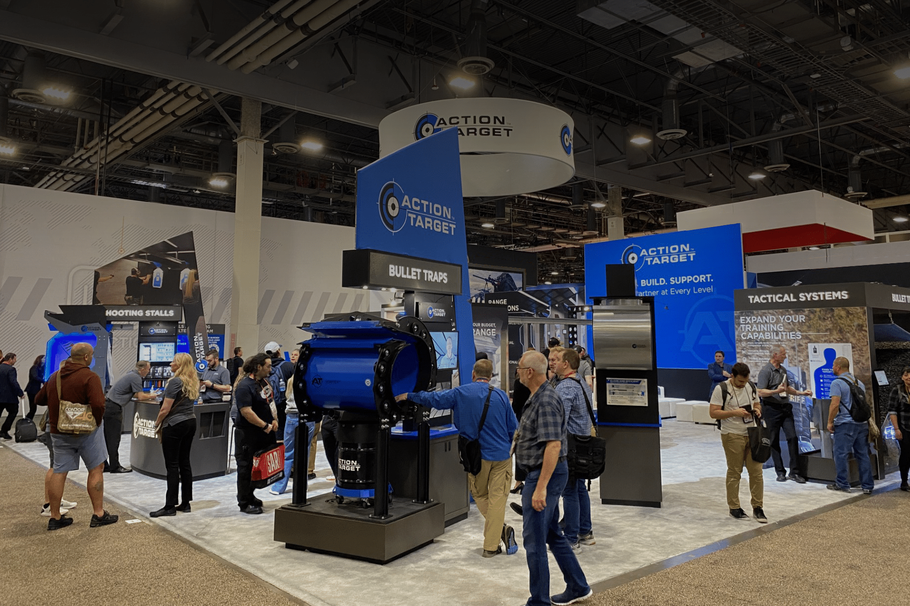 Booth with Action Target branding at trade show, people observing exhibits, indoor convention center.