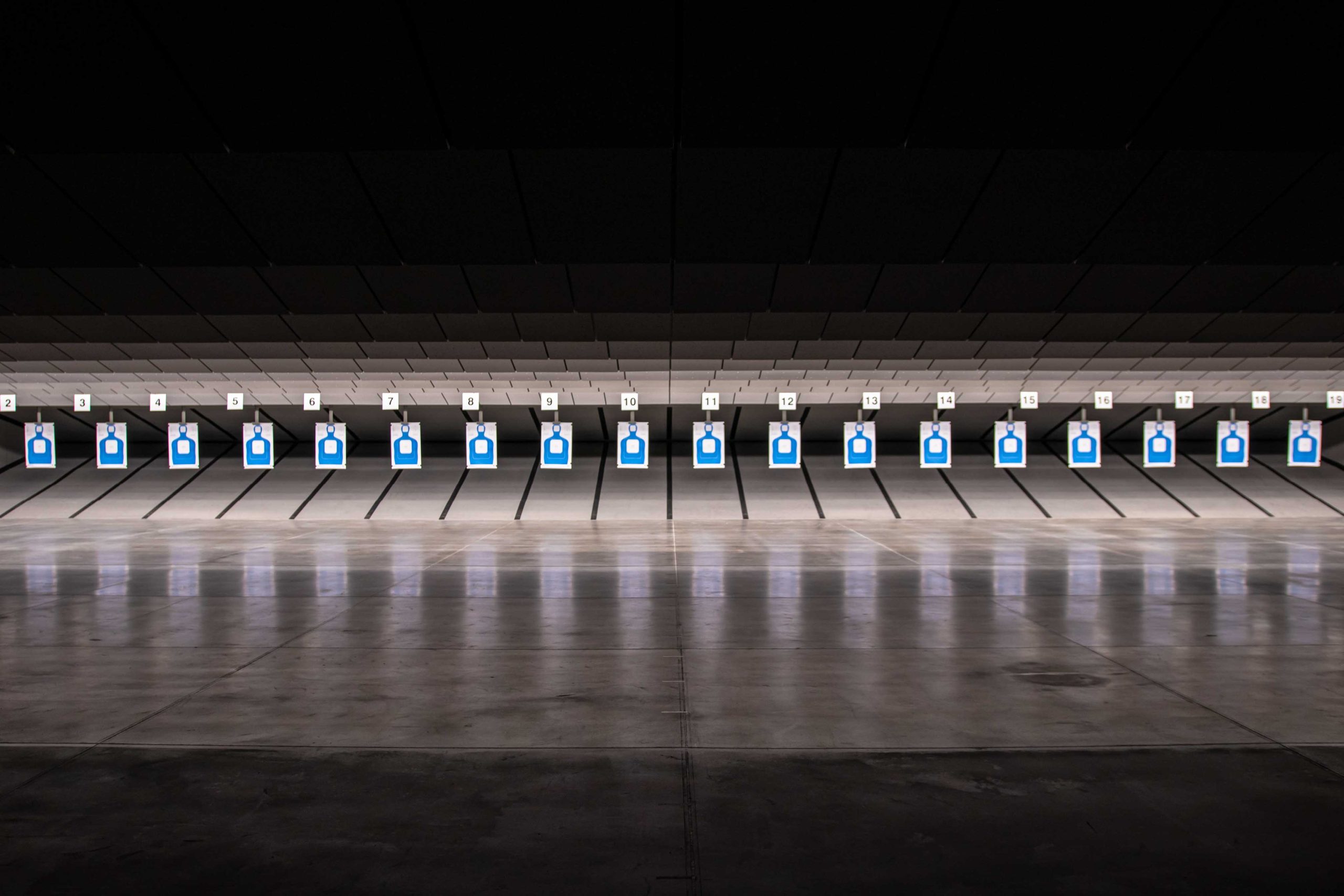 Indoor shooting range with multiple blue silhouette targets in numbered lanes