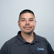 A person stands against a plain background, wearing a dark polo shirt with a logo on the chest.