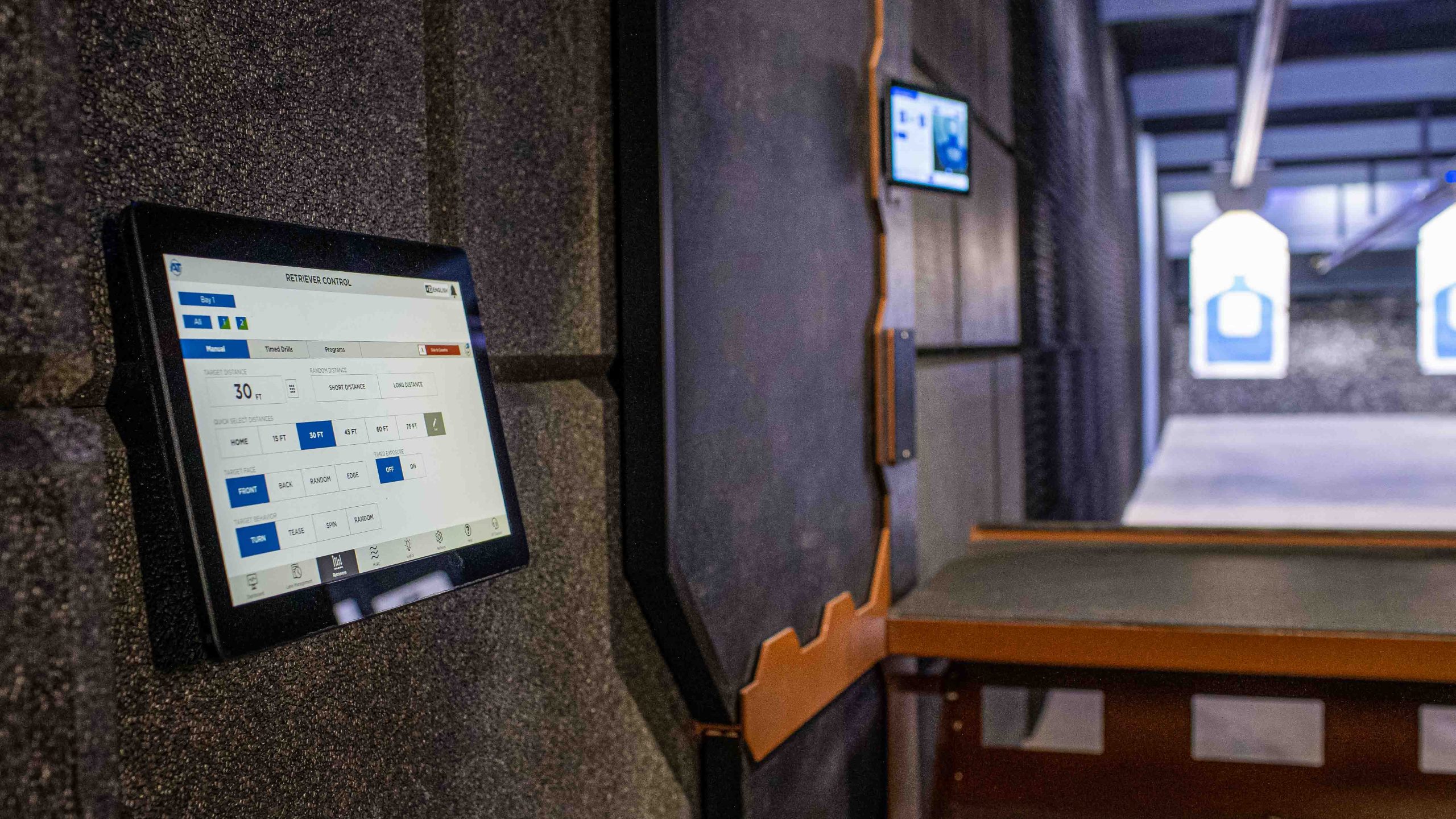 Tablet displays shooting range control options; range stalls and target visible in background.
