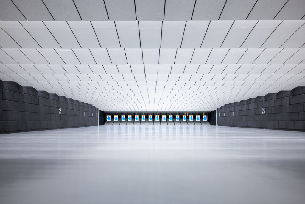 brightly lit indoor shooting range with paper targets hanging